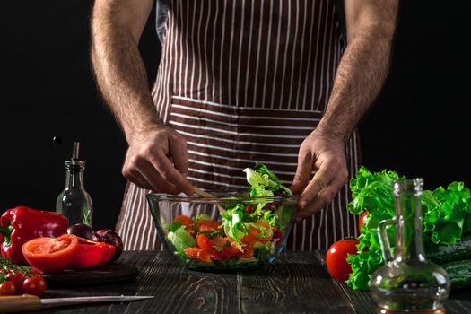 Man preparing salad with fresh vegetables on a wooden table. Cooking tasty and healthy food. On black background. Vegetarian food, healthy or cooking concept.