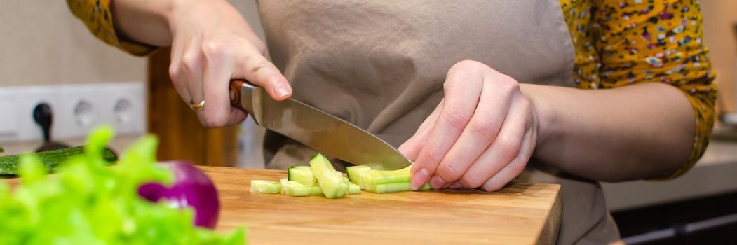 Close-up view of the salad preparation process. A woman in an apron cuts a cucumber on a wooden cutting board. Culinary site header