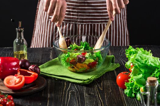 Man preparing salad with fresh vegetables on a wooden table. Cooking tasty and healthy food. On black background. Vegetarian food, healthy or cooking concept.