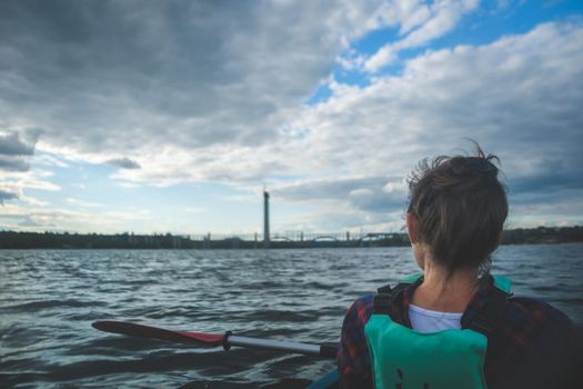 Woman exploring by the river. Young woman on kayak in the sea with blue sky and clouds on background.