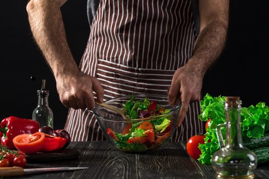 Man preparing salad with fresh vegetables on a wooden table. Cooking tasty and healthy food. On black background. Vegetarian food, healthy or cooking concept.