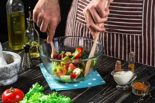 Man preparing salad with fresh vegetables on a wooden table. Cooking tasty and healthy food. On black background. Vegetarian food, healthy or cooking concept.