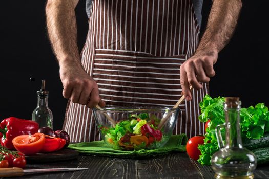 Man preparing salad with fresh vegetables on a wooden table. Cooking tasty and healthy food. On black background. Vegetarian food, healthy or cooking concept.