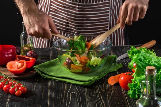 Man preparing salad with fresh vegetables on a wooden table. Cooking tasty and healthy food. On black background. Vegetarian food, healthy or cooking concept.