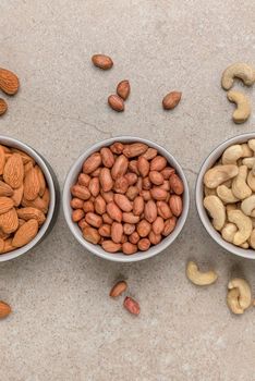 Nuts of different varieties, top view. Vertical photo for background, nuts in bowls on marble table top, place for text or design.