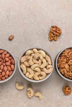 Nuts of different varieties, top view. Vertical photo for background, nuts in bowls on marble table top, place for text or design.