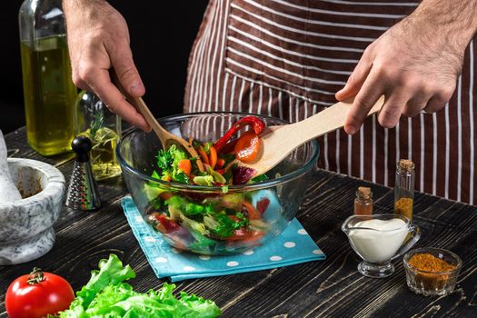 Man preparing salad with fresh vegetables on a wooden table. Cooking tasty and healthy food. On black background. Vegetarian food, healthy or cooking concept.