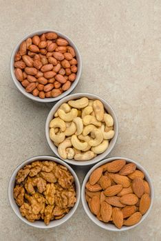 Nuts of different varieties, top view. Vertical photo for background, nuts in bowls on marble table top, place for text or design.