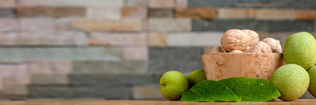 Walnut. Walnut fruits lie in a wooden saucer. Nearby are green leaves and unripe walnut fruits. Banner, copy space or paste text