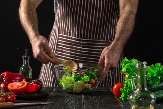 Man preparing salad with fresh vegetables on a wooden table. Cooking tasty and healthy food. On black background. Vegetarian food, healthy or cooking concept.