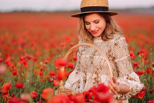 a girl in a dress with a hat and with a basket in a field with poppies.