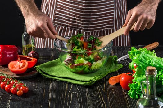 Man preparing salad with fresh vegetables on a wooden table. Cooking tasty and healthy food. On black background. Vegetarian food, healthy or cooking concept.