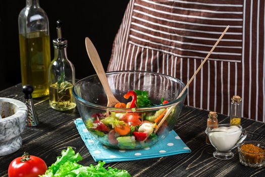 Man preparing salad with fresh vegetables on a wooden table. Cooking tasty and healthy food. On black background. Vegetarian food, healthy or cooking concept.