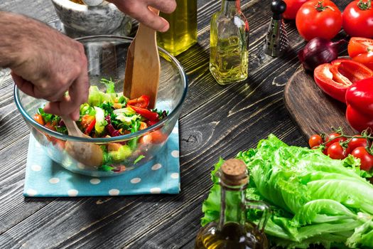 Man preparing salad with fresh vegetables on a wooden table. Cooking tasty and healthy food. On black background. Vegetarian food, healthy or cooking concept. Close-up