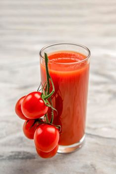 A glass of tomato juice and a branch of small tomatoes. Cherry tomatoes in a red plate on a marble background. Place to insert text or design