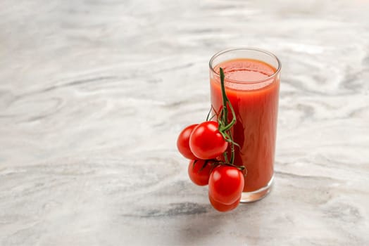 A glass of tomato juice and a branch of small tomatoes. Cherry tomatoes in a red plate on a marble background. Place to insert text or design