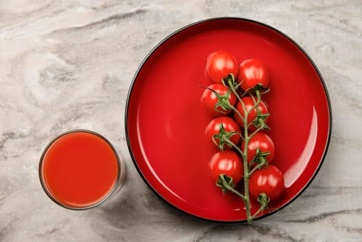 A glass of tomato juice and a branch of small tomatoes. Cherry tomatoes in a red plate on a marble background. Place to insert text or design