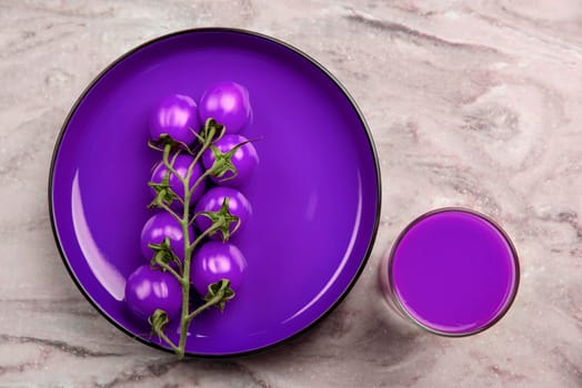 A glass of tomato juice and a branch of small purple tomatoes. Cherry tomatoes in a red plate on a marble background. Place to insert text or design