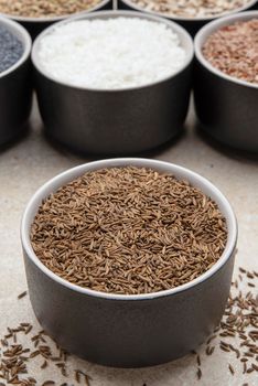 Caraway seeds. Cup with caraway seeds on a background of various seeds in black containers on a marble table top.