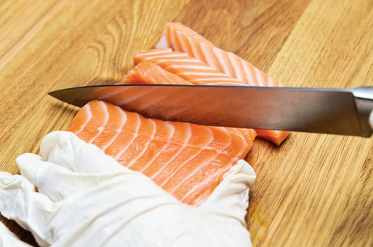 Chef's hands close up. On a wooden cutting board, the chef cuts a red fish with a knife. Salmon for Japanese sushi