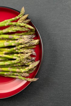 Green asparagus on a black slate stone background. Top view, asparagus in a red plate. Culinary banner with place for text