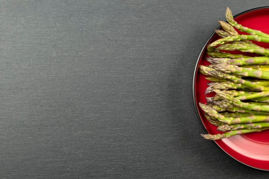 Green asparagus on a black slate stone background. Top view, asparagus in a red plate. Culinary banner with place for text
