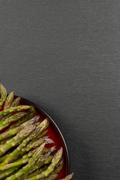 Green asparagus on a black slate stone background. Top view, asparagus in a red plate. Culinary banner with place for text