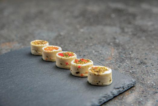 Cheese platter with spices. Mazzarella cheese with different spices. Cheese snacks of various flavors on a black stone tray. background or banner on the theme of food and snacks.