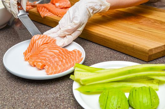 Chef's hands close up. On a wooden cutting board, the chef cuts a red fish with a knife. Salmon for Japanese sushi