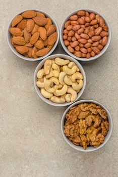 Nuts of different varieties, top view. Vertical photo for background, nuts in bowls on marble table top, place for text or design.