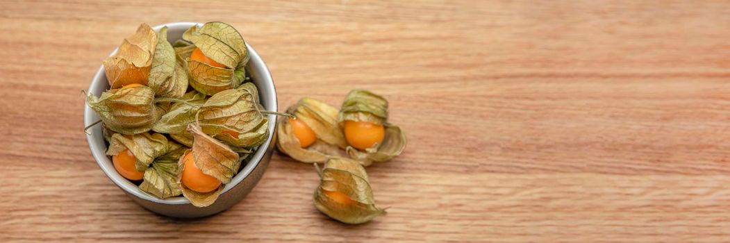 Physalis fruits on a wooden table. Sweet yellow physalis berries in a cup on wood background.