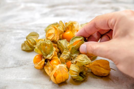 Physalis in hand. The hand takes the sweet yellow physalis berries, the ripe physalis fruits lie on the marble tabletop. Place for your text , for design or product label.