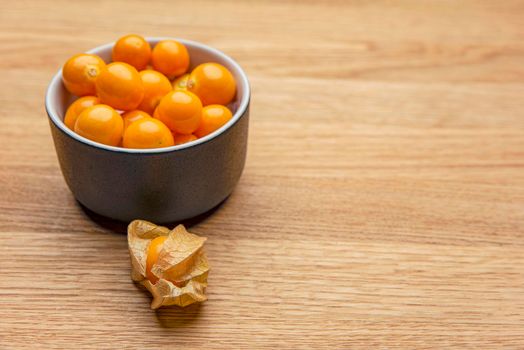 Physalis fruits on a wooden table. Sweet yellow physalis berries in a cup on wood background.