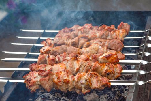 Grilled pork meat on metal skewers. Barbecue cooking. The smoke from the coals develops over the meat. Promotional banner for menu with copy space to insert text.