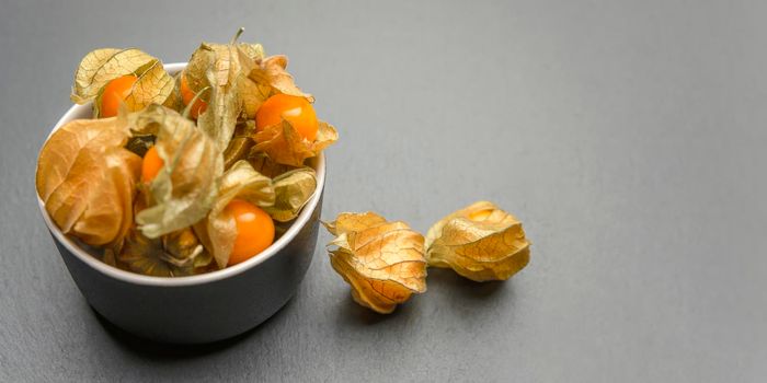 Physalis fruits against black background. Sweet yellow physalis berries in a cup on a dark table top, place to insert text or design.