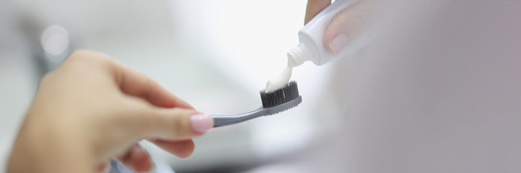 Close-up of person apply toothpaste on toothbrush, preparing to clean teeth in bathroom. Get ready, morning routine, hygiene, body and face care concept. Blurred background