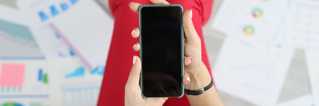 Top view of woman holding phone with black screen, turn off device, no connection, broken smartphone, mockup. Technology, work collapse, damage concept. Copy space. Blurred background