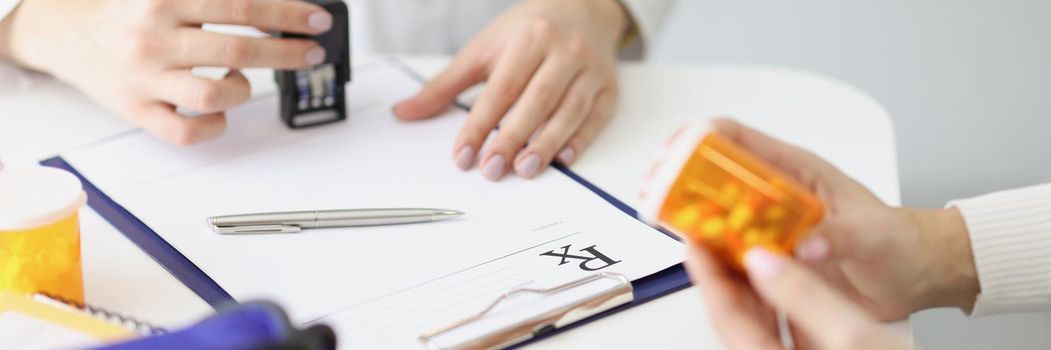 Close-up of doctor make stamp on prescription paper, patient hold bottle with medication. Planned appointment at doctor in clinic, tablets for recovery. Medicine, checkup, health concept