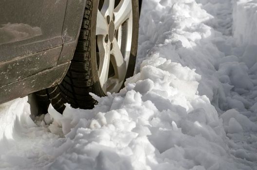 Closeup of the car tire on winter road covered with snow. Snowflakes are on the rubber wheel