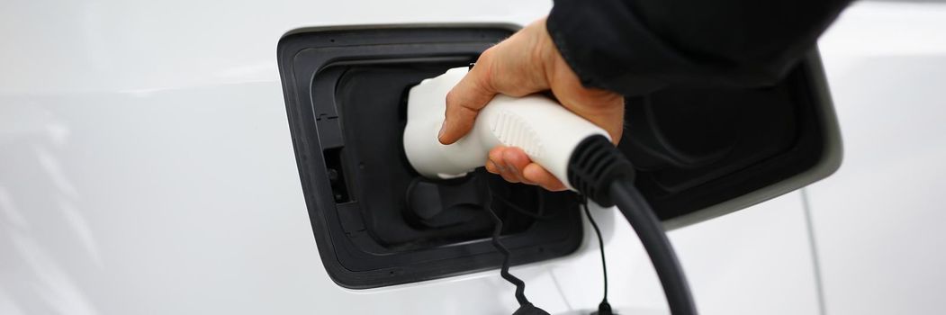 Close-up of hand holding fuel nozzle to add gas at petrol station, refueling car with diesel. Clean white automobile on parking. Vehicle, maintenance, transportation, ownership concept