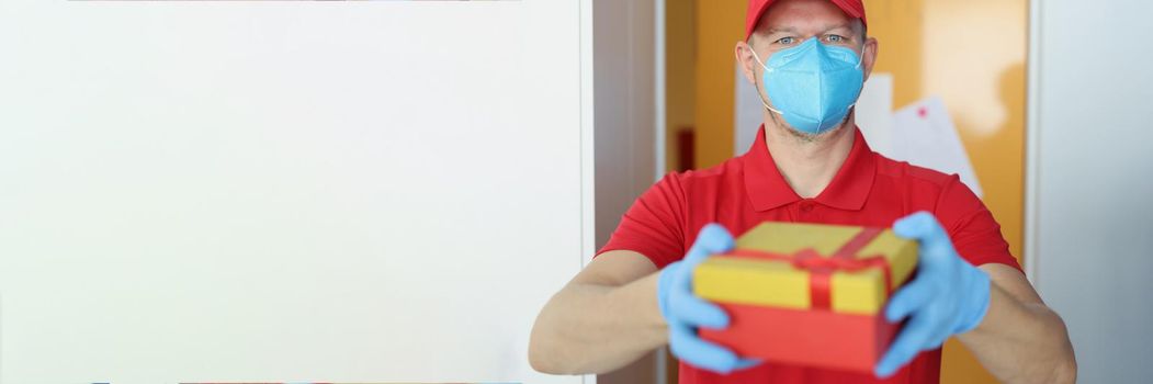 Portrait of courier man wearing face mask, safe delivery during pandemic times. Worker in uniform deliver decorated package to receiver. Delivery service, quarantine, protection concept