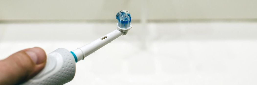Rechargeable, electric toothbrush, close-up. Against the backdrop of a bathroom in white. Water faucet and white sink.
