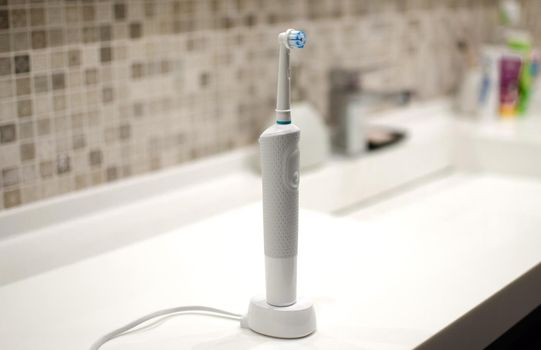 Rechargeable, electric toothbrush, close-up. Against the backdrop of a bathroom in white. Water faucet and white sink.