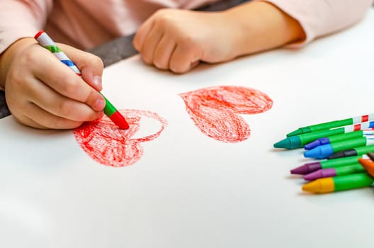 A little girl is drawing a heart with red chalk - high angle image with selective focus. Valentine's day concept.