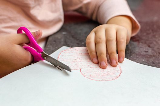 The girl's hand holds a heart cut from paper. Children's creativity - drawings and crafts for Valentine's Day or Mother's Day