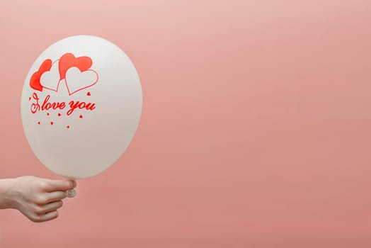 Valentine's card with place for text. Balloon with the inscription love in the child's hand. On a pink background.