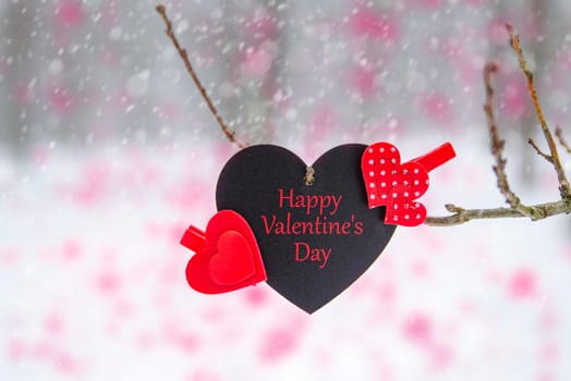 Happy Valentine's Day greeting card or banner. Red hearts on a branch of a snow-covered tree in winter. Holidays Happy Valentine's Day. Snowfall on the background of the forest.
