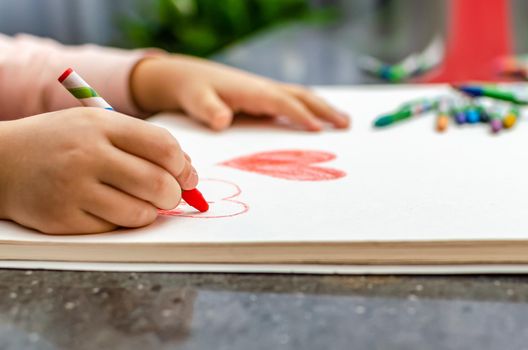 A little girl is drawing a heart with red chalk - high angle image with selective focus. Valentine's day concept.