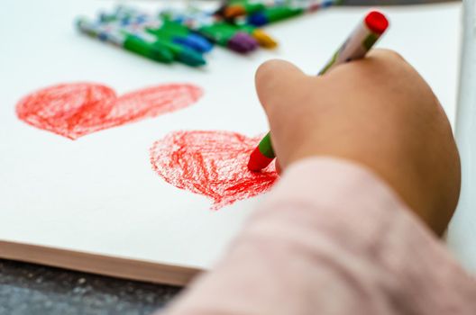 A little girl is drawing a heart with red chalk - high angle image with selective focus. Valentine's day concept.