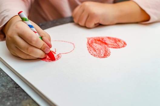 A little girl is drawing a heart with red chalk - high angle image with selective focus. Valentine's day concept.